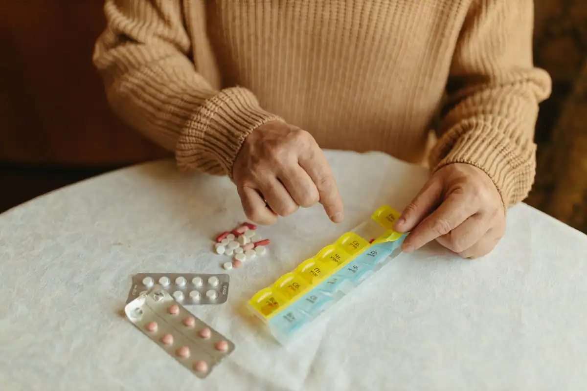 Persoană în vârstă care își împarte pastilele zilnice într-un organizator săptămânal