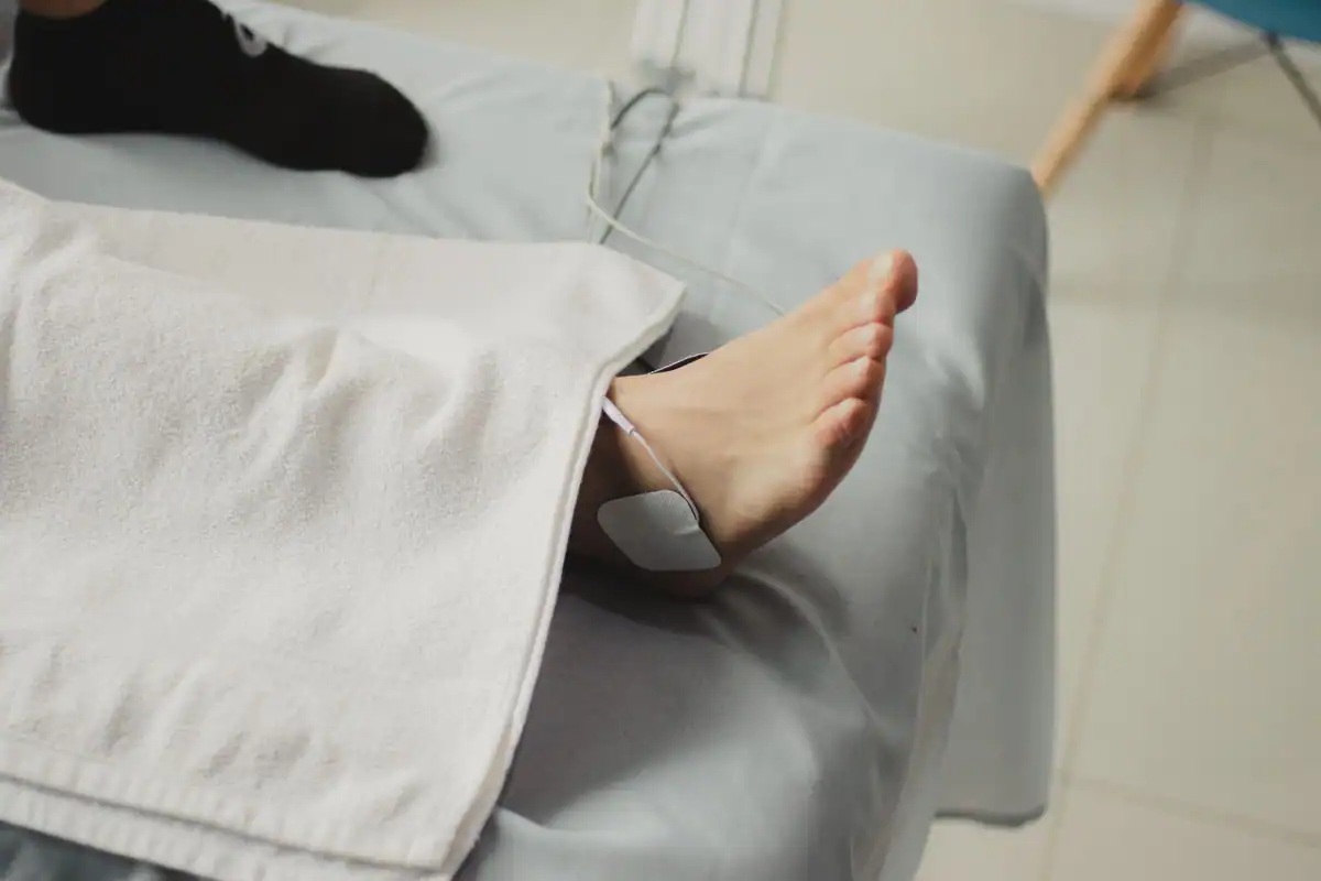 Pacient întins pe pat de tratament, cu electrod de fizioterapie pe picior