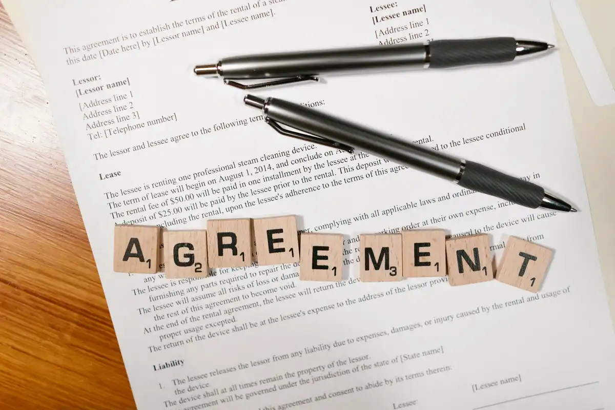 Contract de închiriere cu litere de lemn care formează cuvântul agreement și pixuri