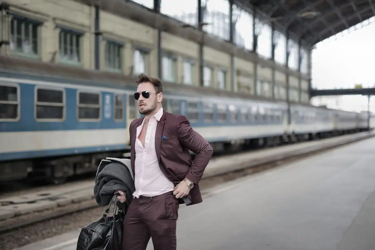 Bărbat elegant cu geantă de voiaj pe peronul unei gări, lângă tren