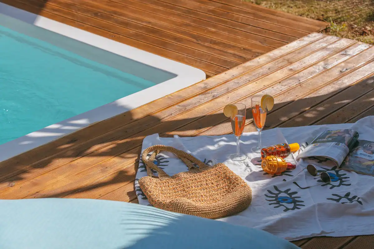Zi însorită la piscină, cu băuturi, reviste și accesorii de vară pe o terasă de lemn