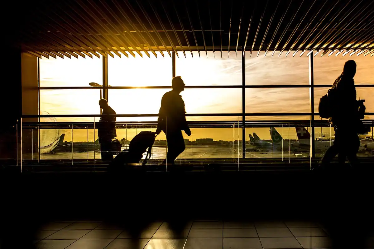 Siluete de călători cu bagaje într-un terminal de aeroport la apus