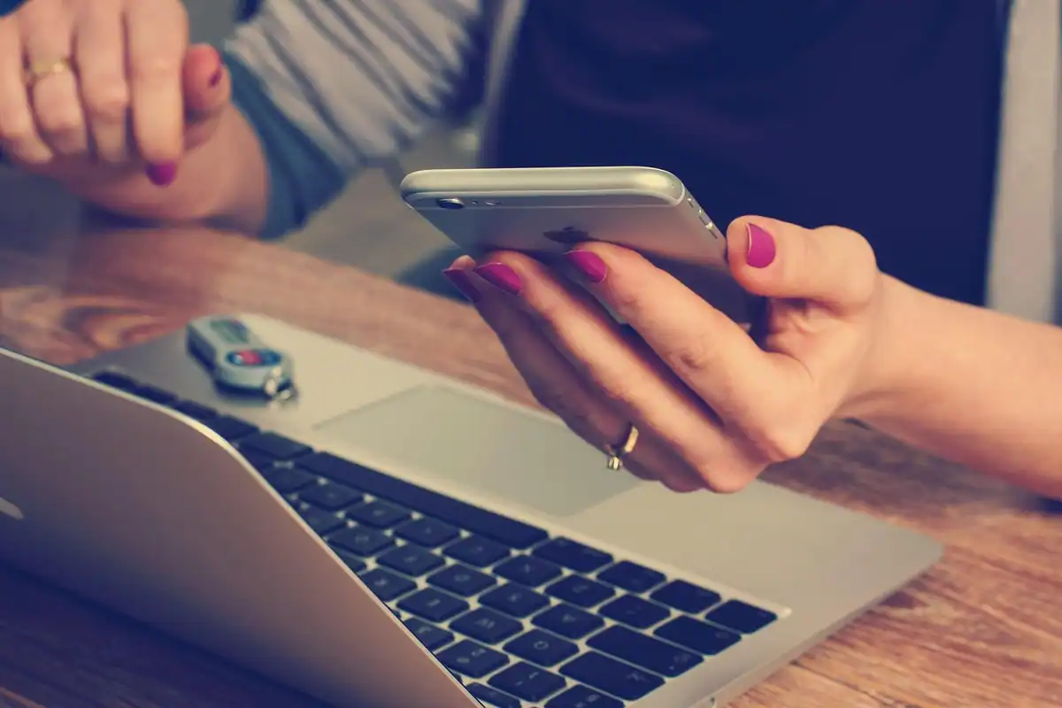 Femeie care rezervă o călătorie online, cu telefonul în mână lângă laptop