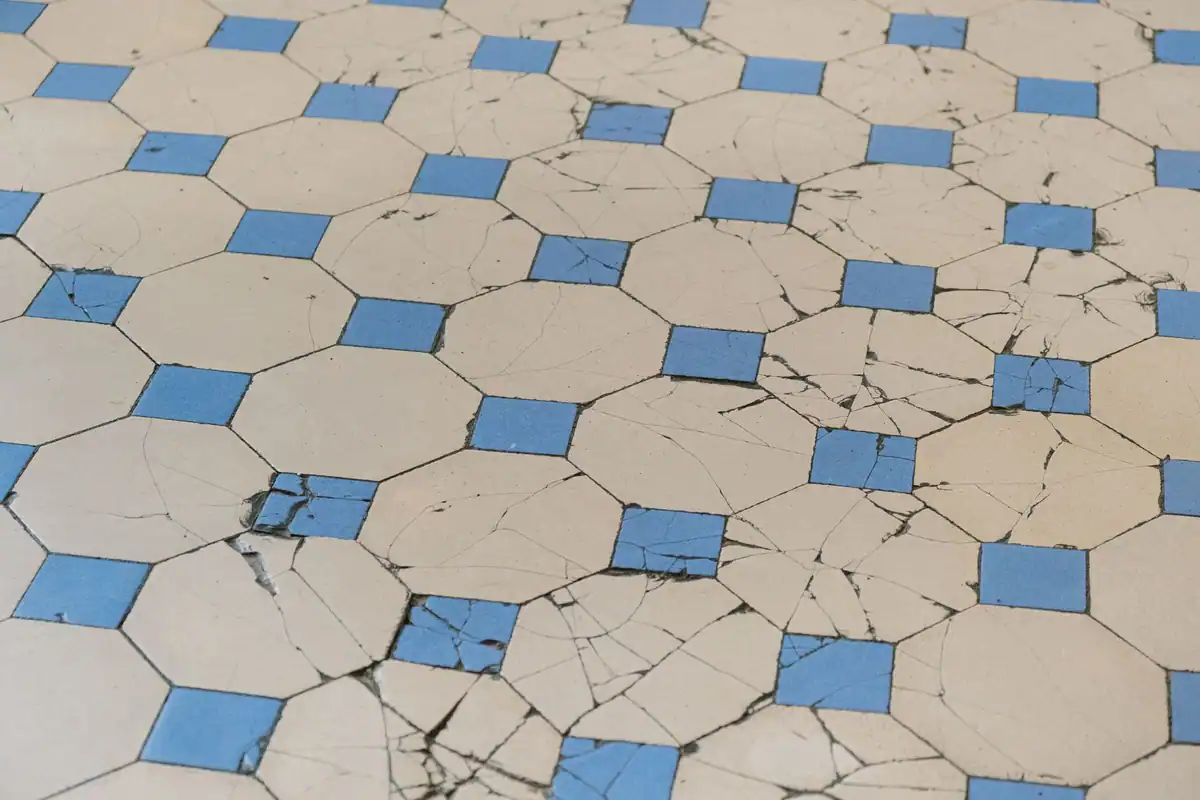 Gresie veche crăpată, cu model geometric albastru, deteriorare a pardoselii