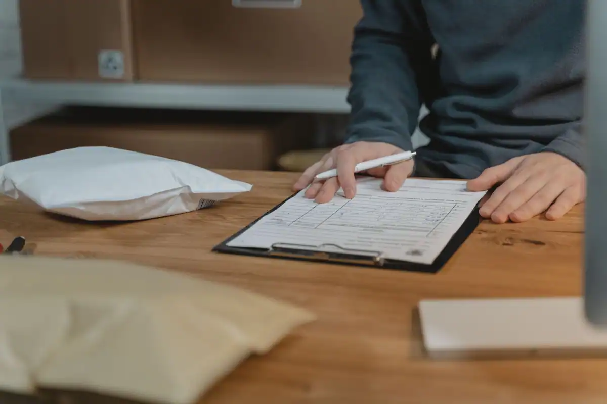 Persoană care completează un formular pe clipboard, la o masă de lemn