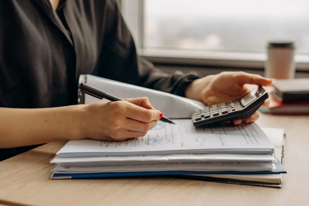Femeie care calculează despăgubirea cu un calculator, peste un teanc de acte