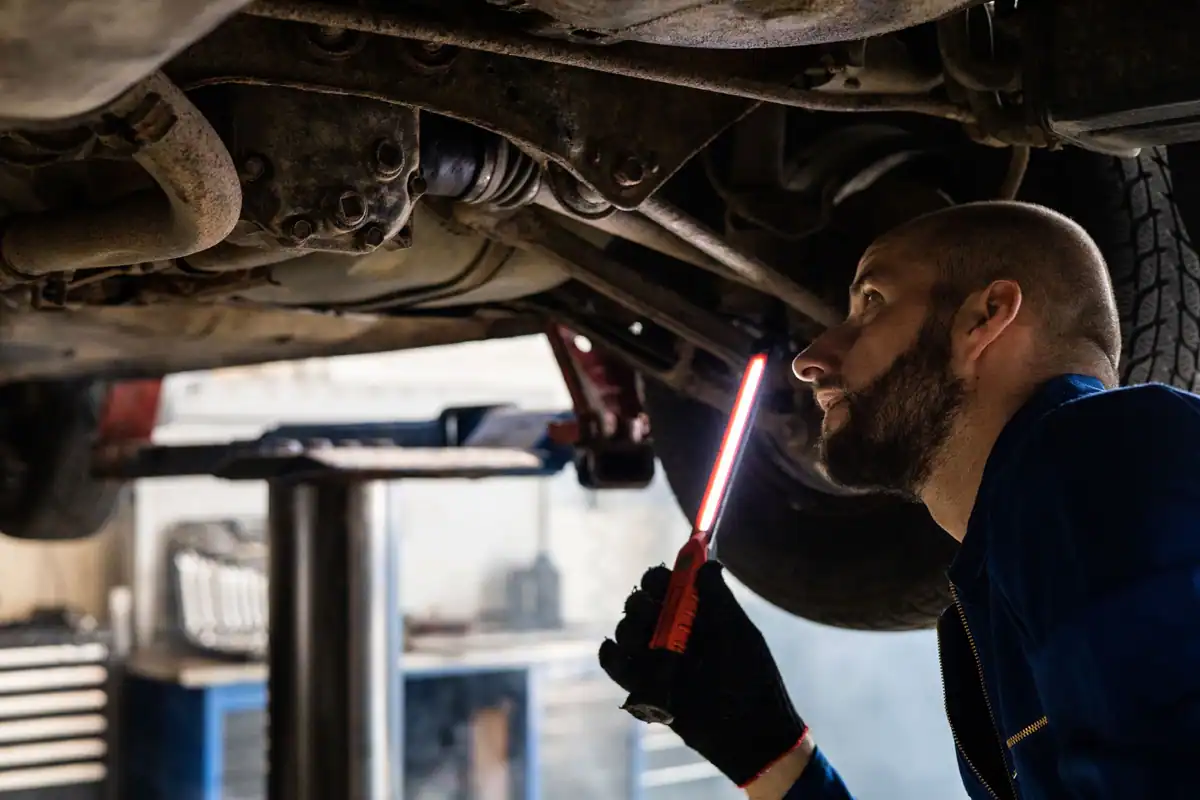 Mecanic care inspectează cu o lanternă partea inferioară a unui vehicul într-un atelier