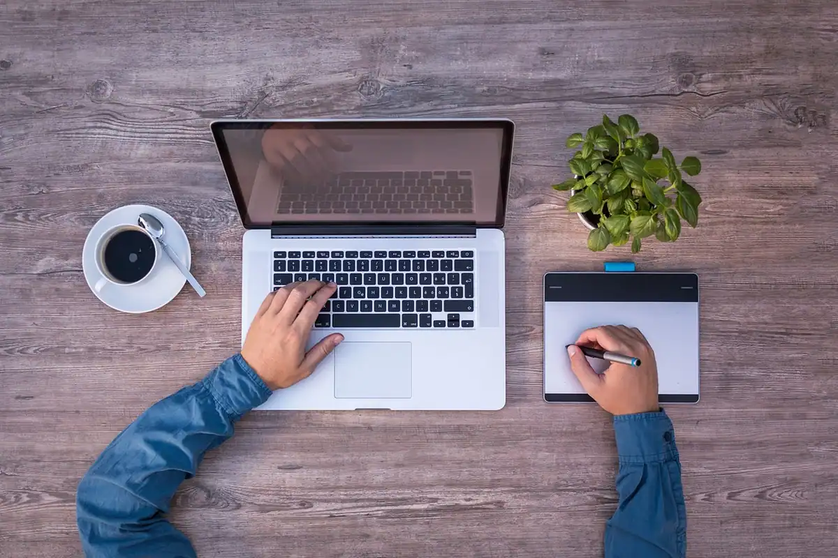 Bărbat care lucrează la laptop pe un birou de lemn, lângă o cafea