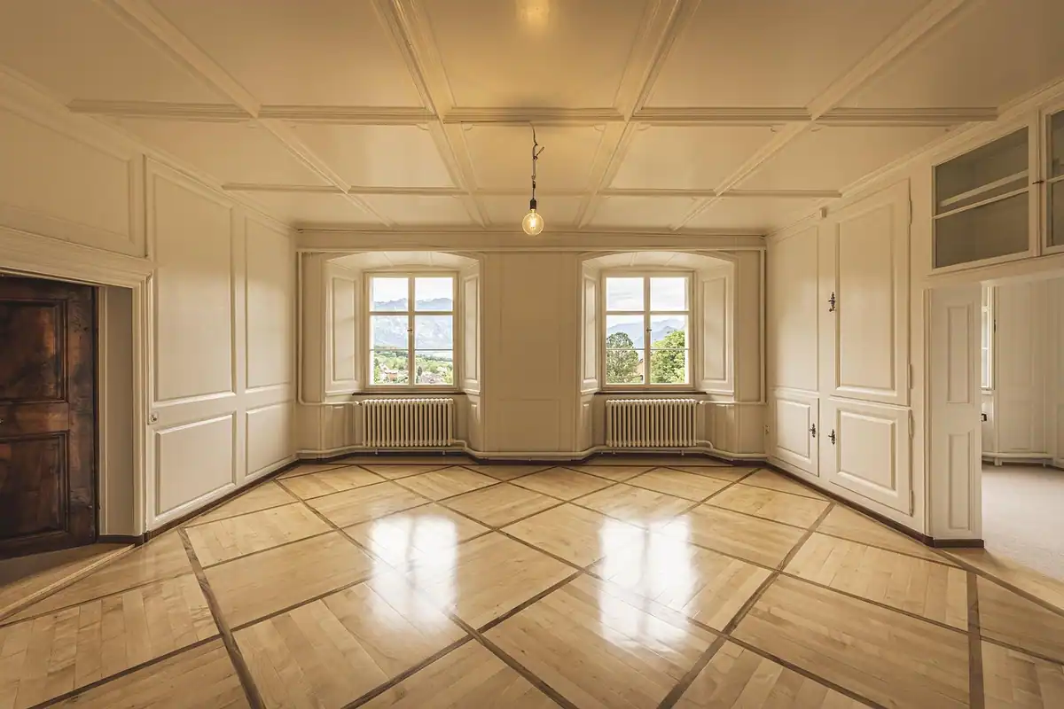 Cameră goală dintr-un apartament vechi, cu parchet și calorifere sub ferestre