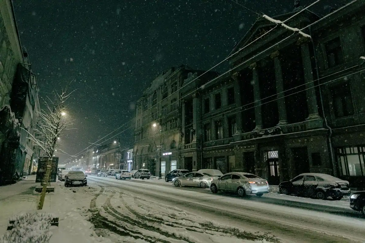 Stradă înzăpezită noaptea, cu mașini parcate lângă clădiri istorice