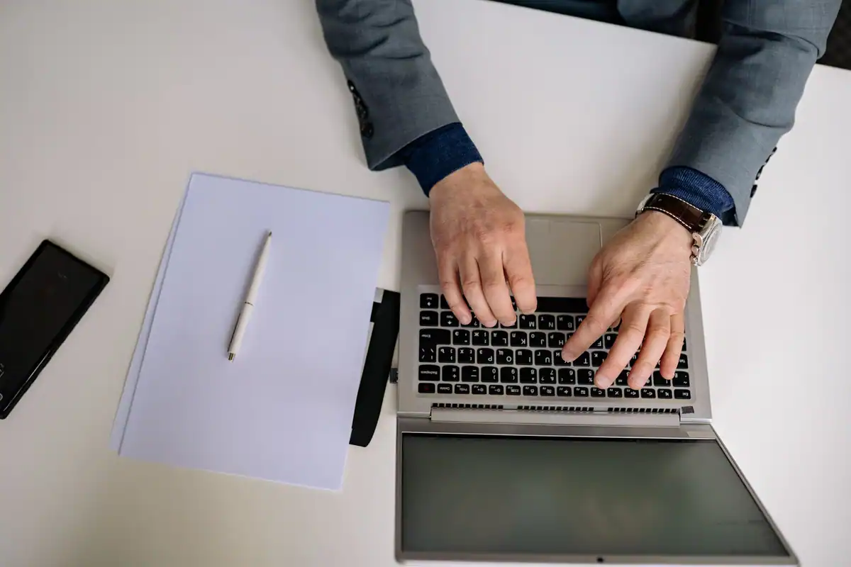 Bărbat la costum care redactează un document pe laptop, văzut de sus